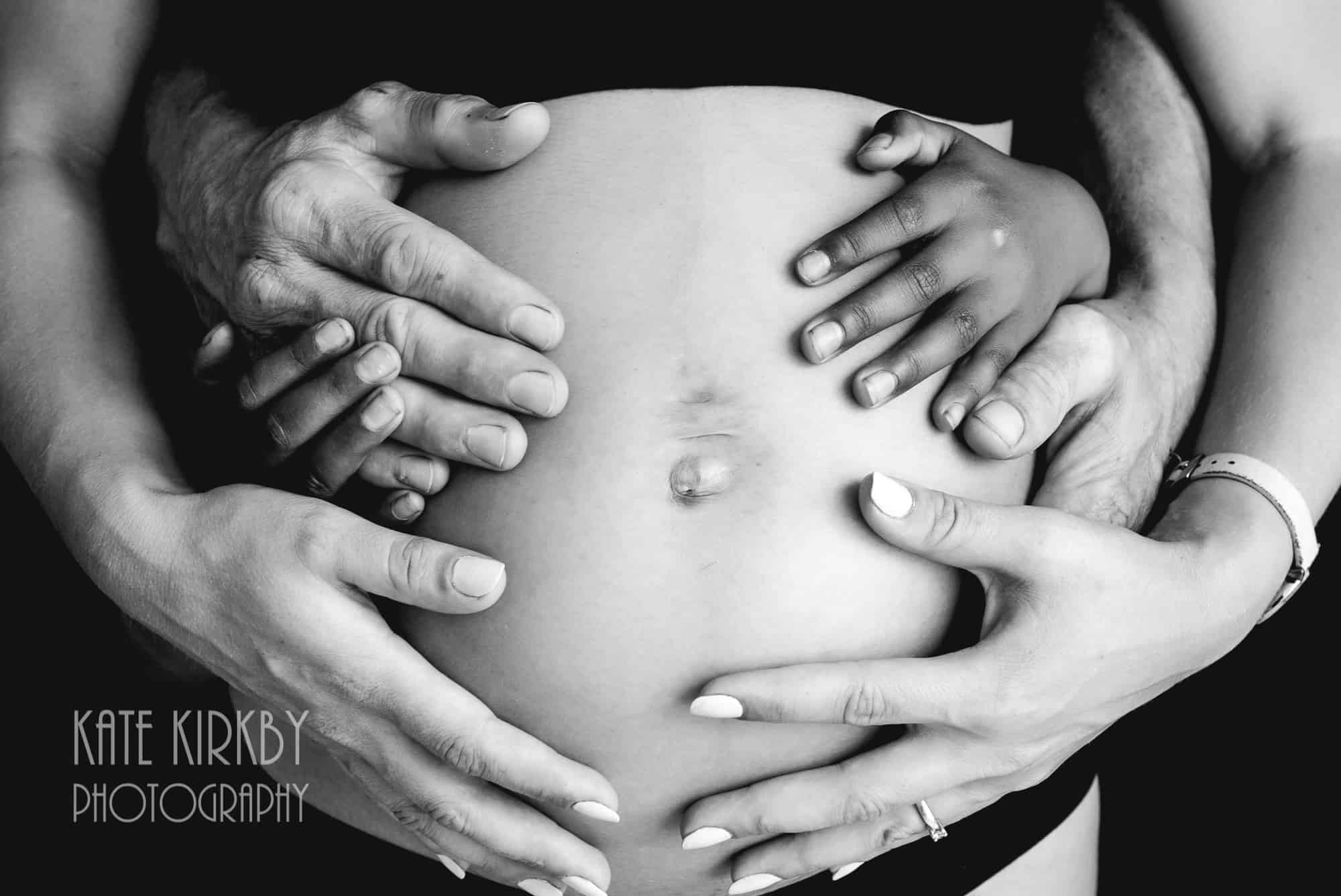 close up of pregnant belly with mum, dad and sisters hands