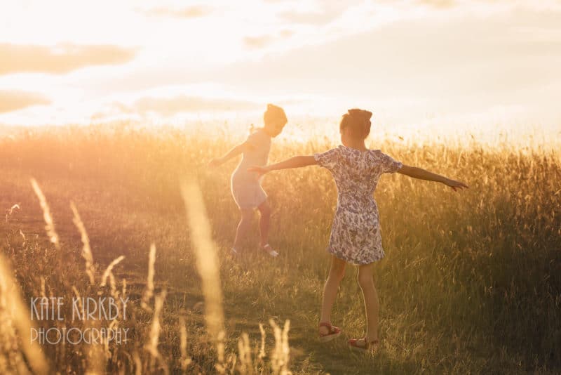girls dancing in long grass at sunset taken by outdoor family photographer in bristol