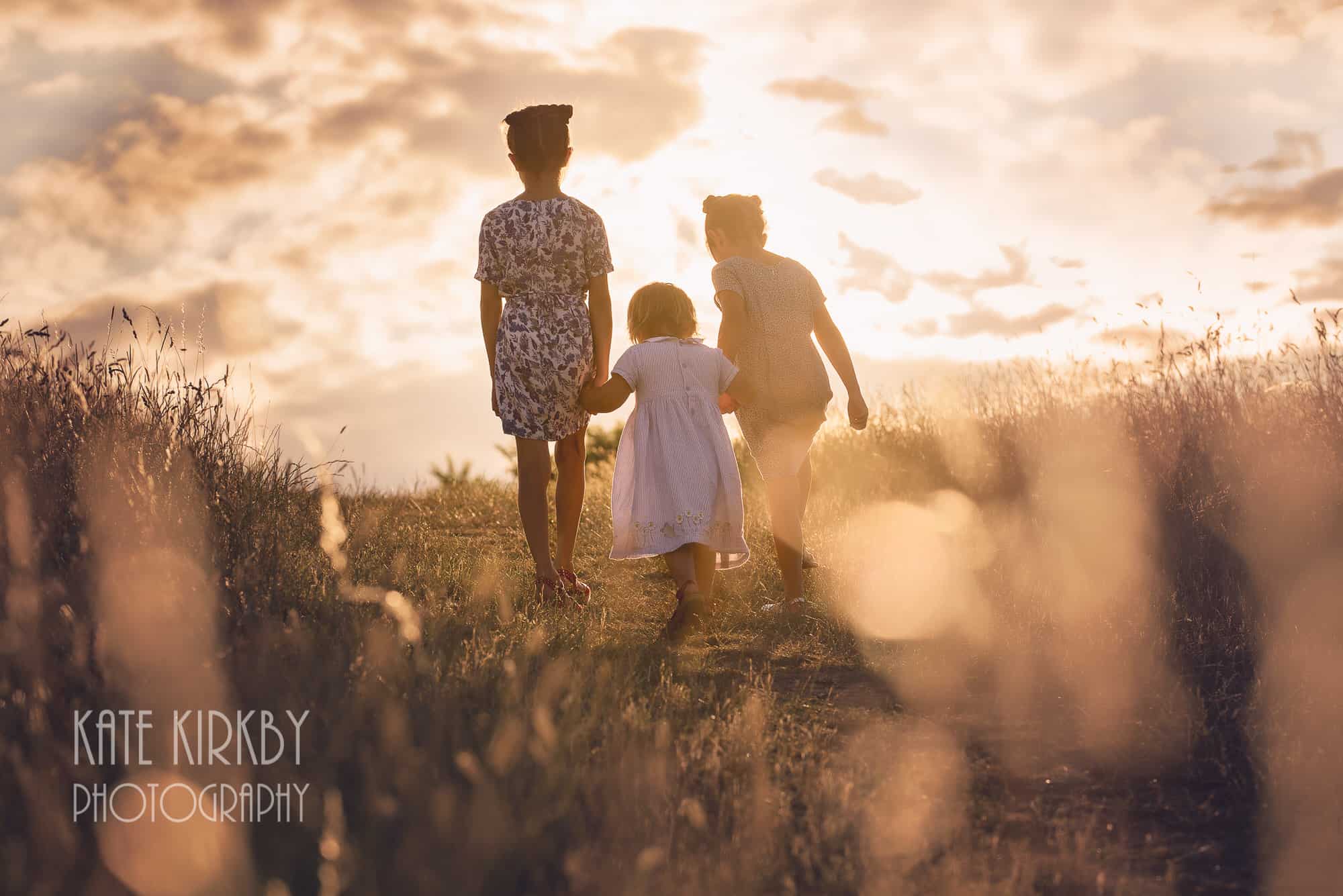 three sisters walking through long summer grass at golden hour