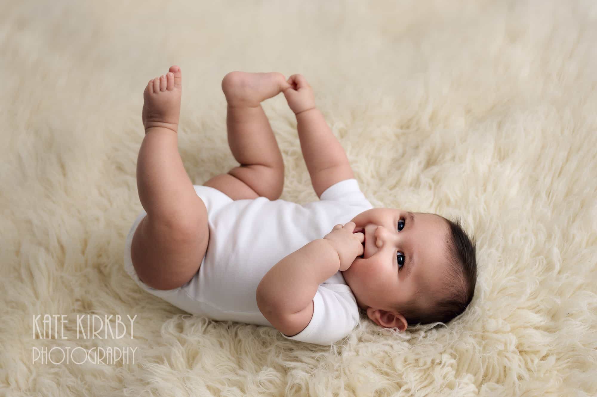 6 month old baby on cream fluffy rug holing his toes