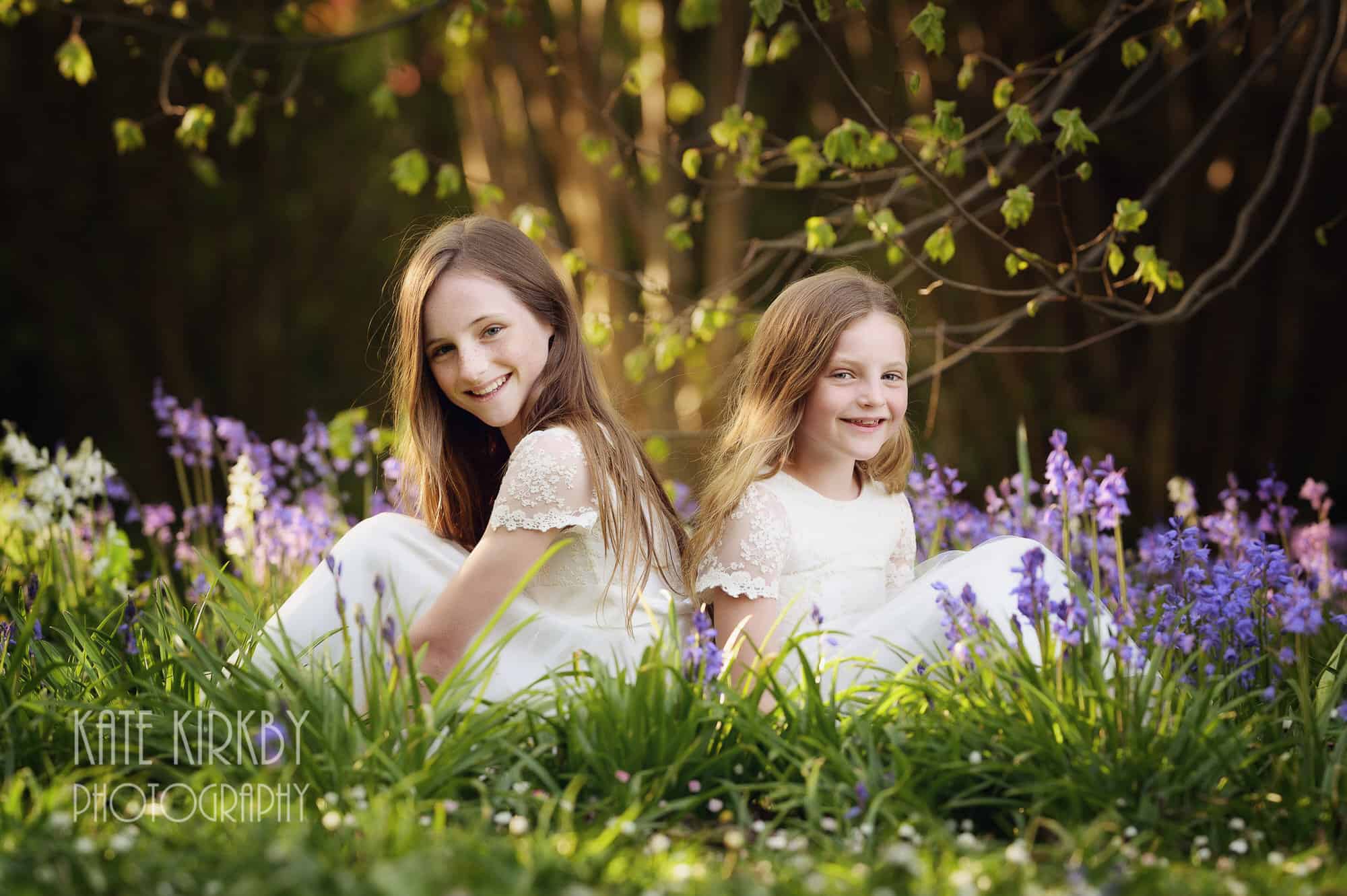 sisters in white dresses sitting in bluebells