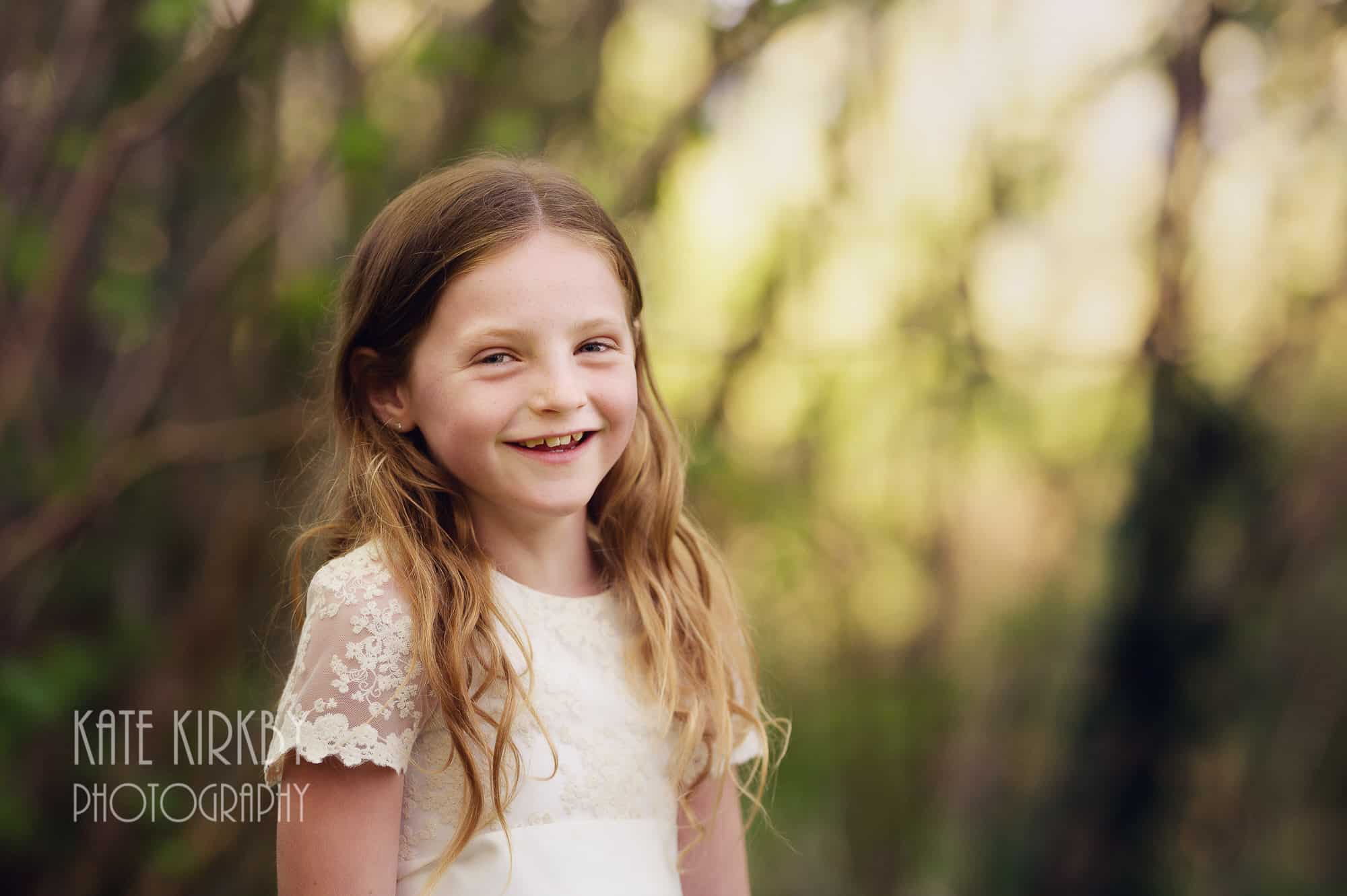 girl in white dress in woodland, smiling at camera