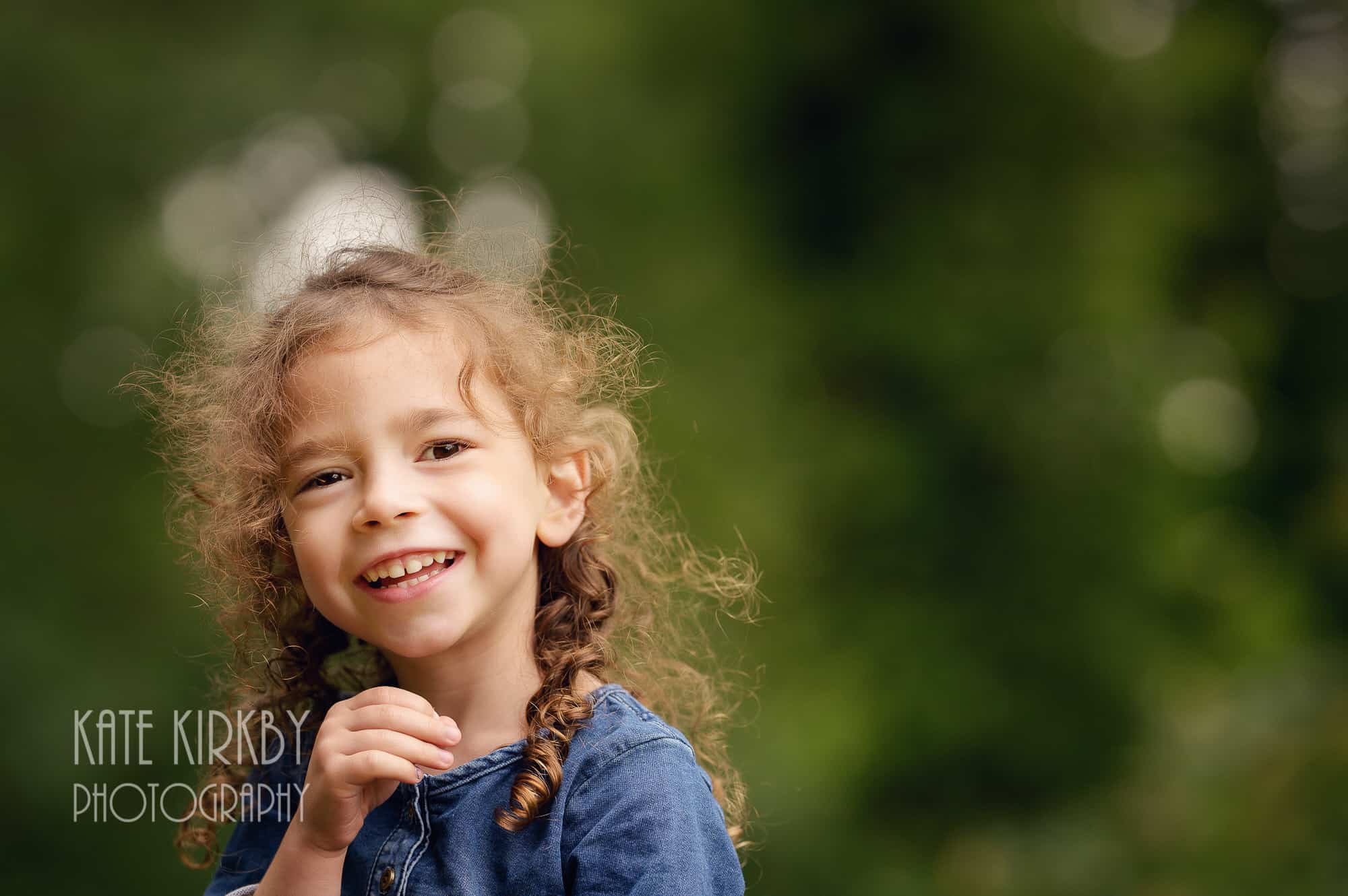 5 year old girl with long brown curls smiling at camera
