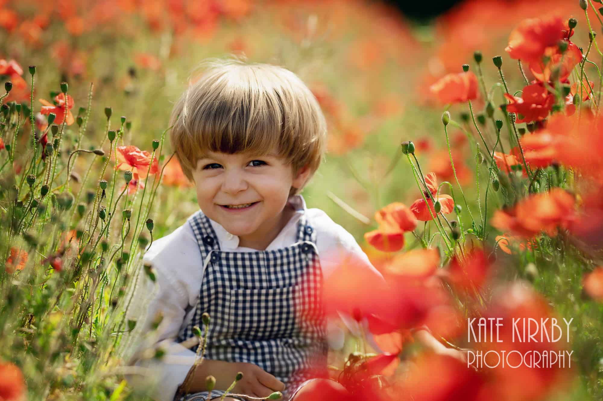 boy in checked dungerees sitting in field of red poppies