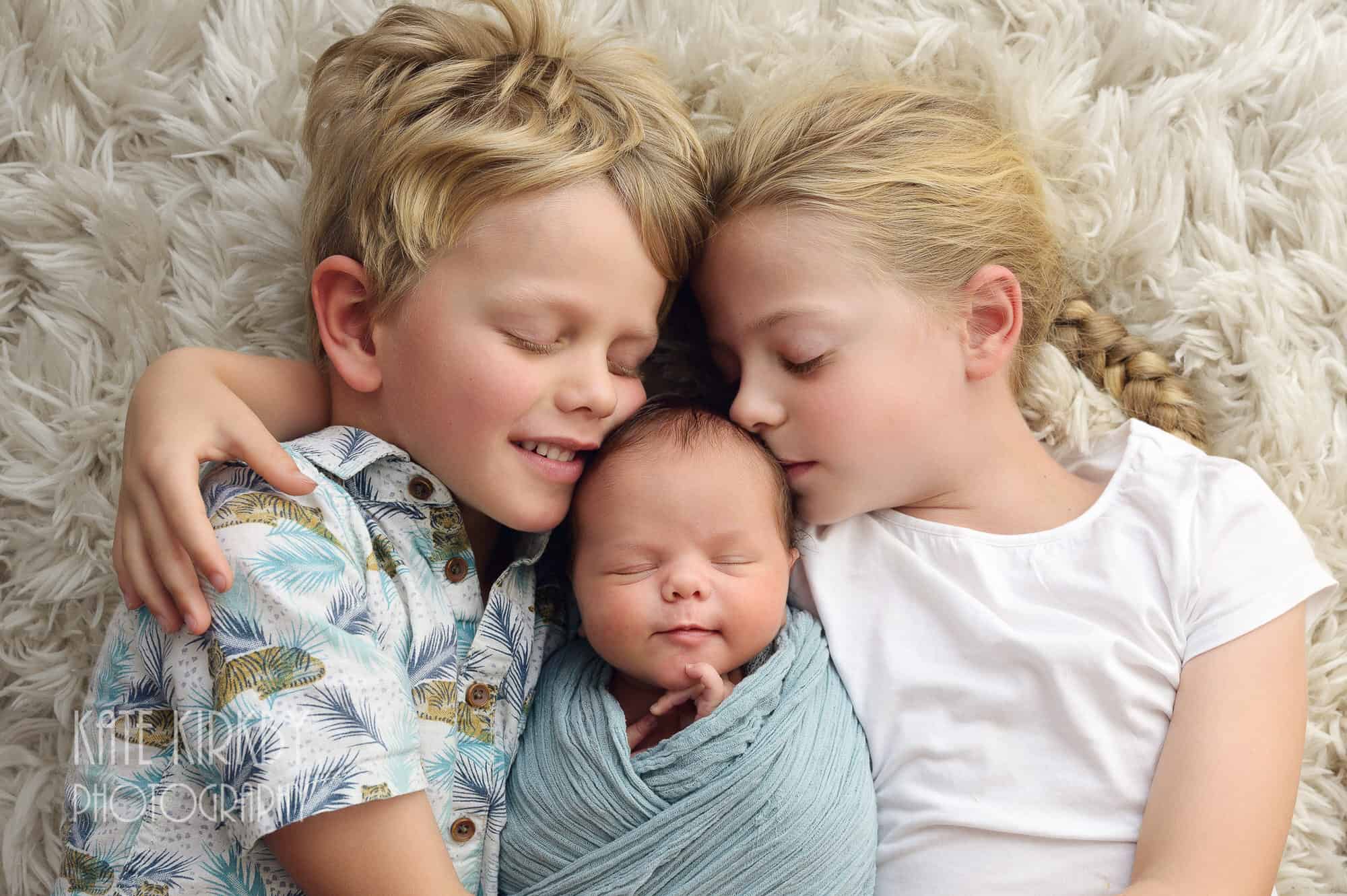 Siblings cuddling newborn