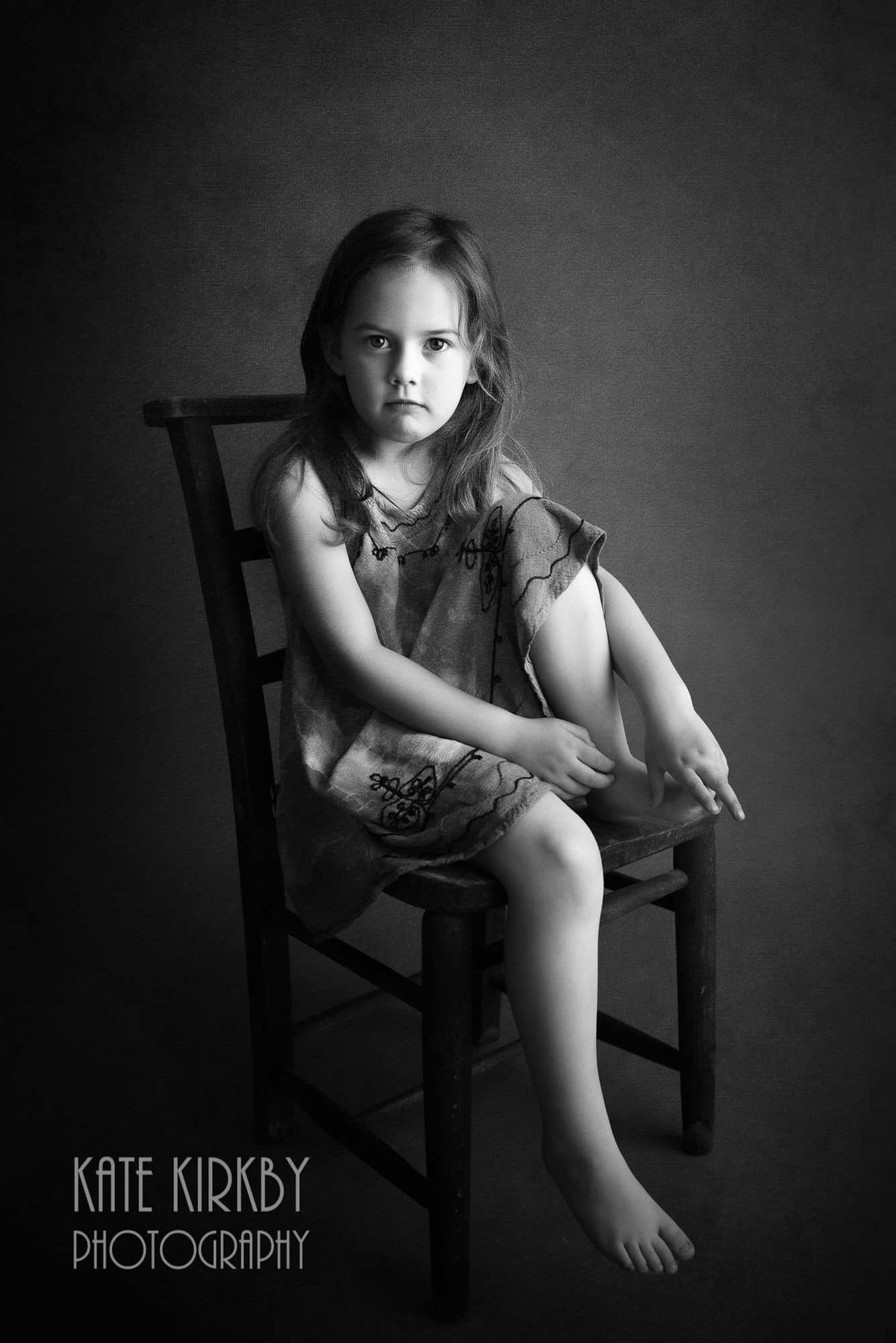 black and white photo of girl sitting on chair looking directly at camera with serious expression