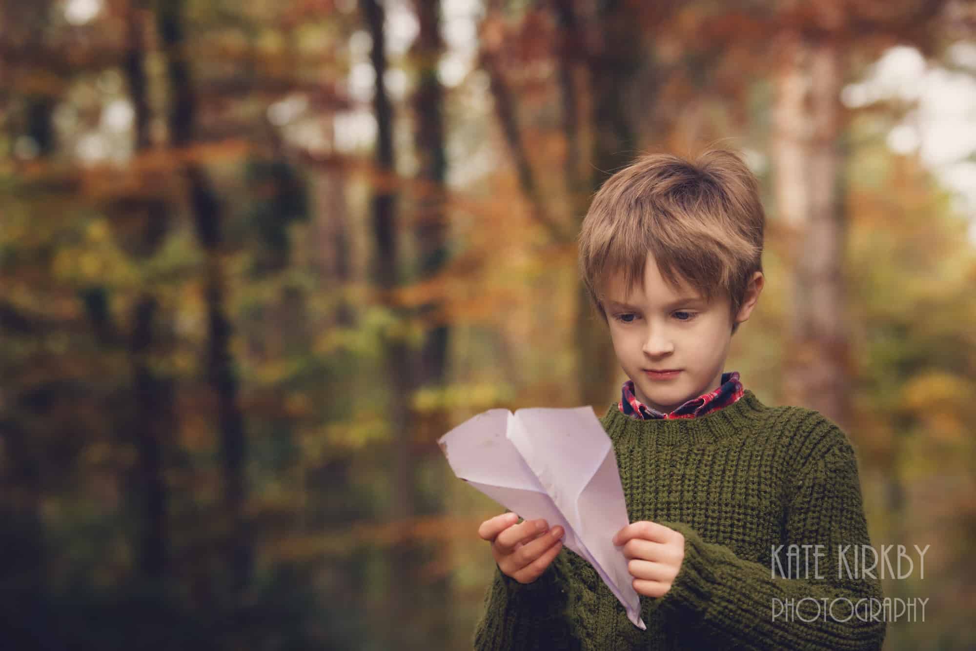 boy plaing with paper aeroplane in woods