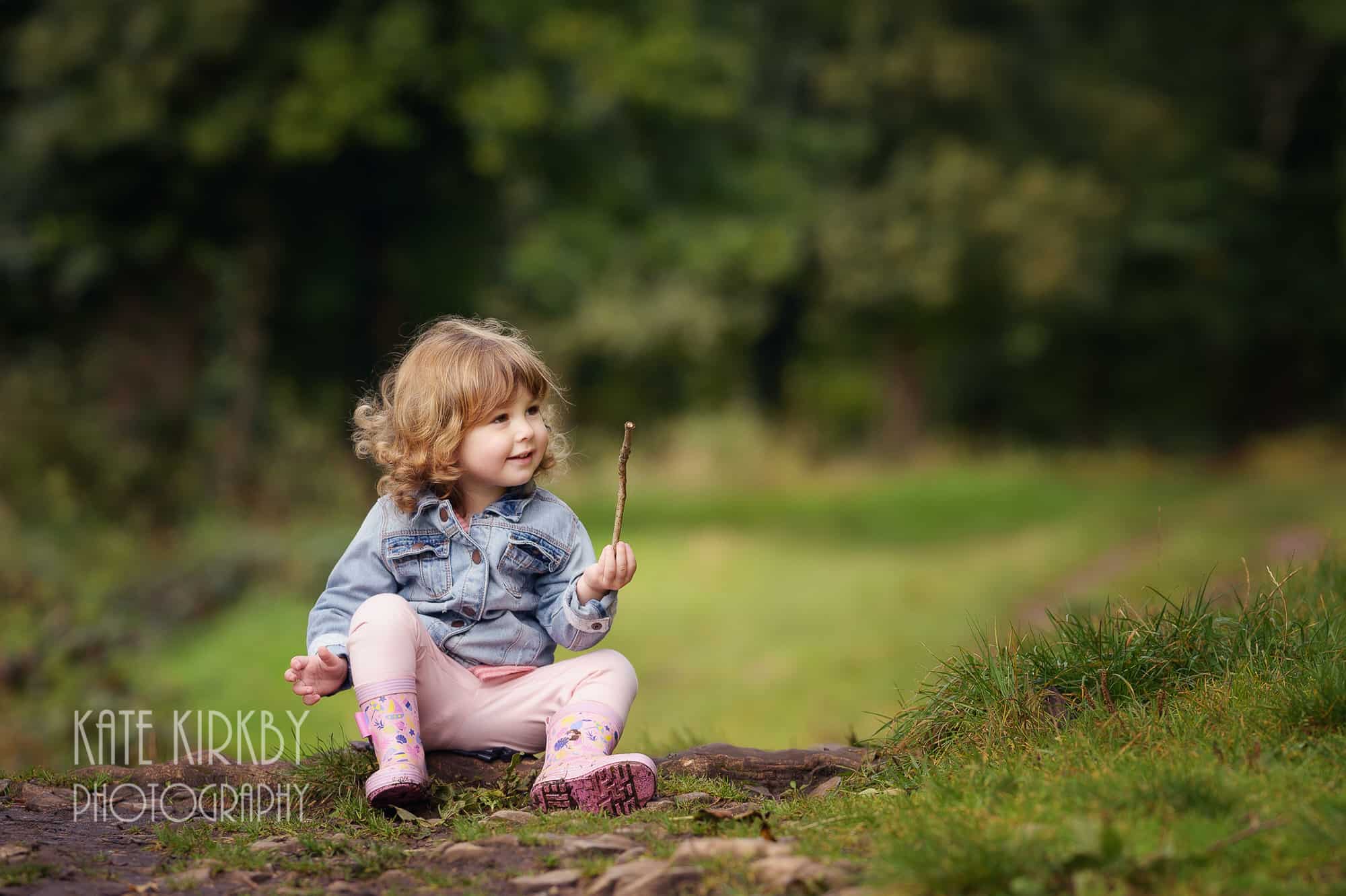 2 year old girl in demin jacket playing with stick