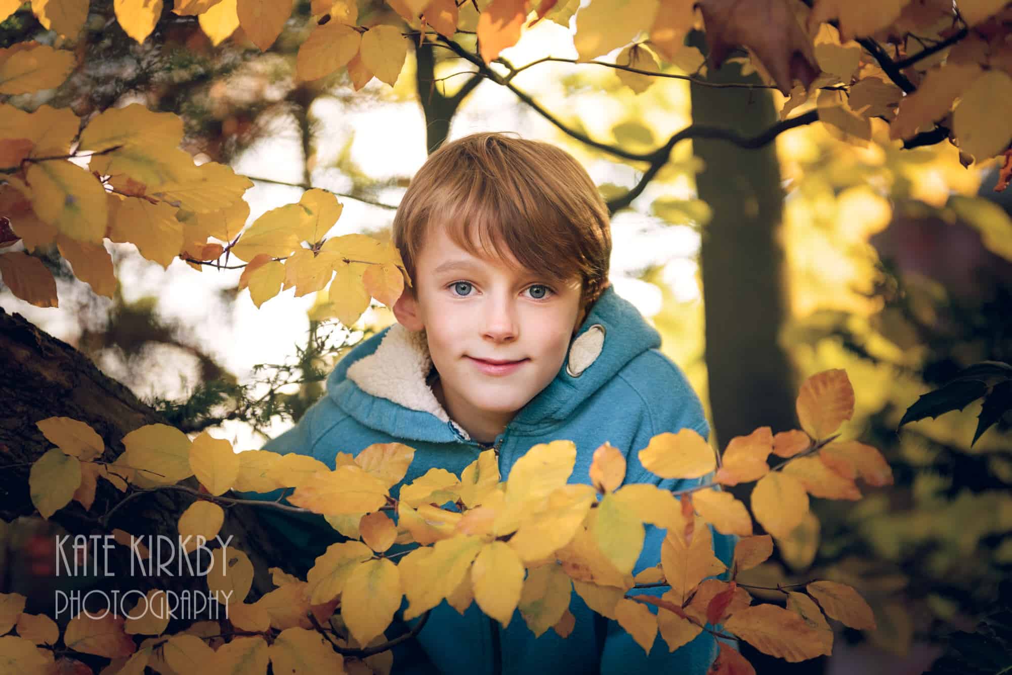 7 year old boys in blue jumper looking through yellow autumn leaves