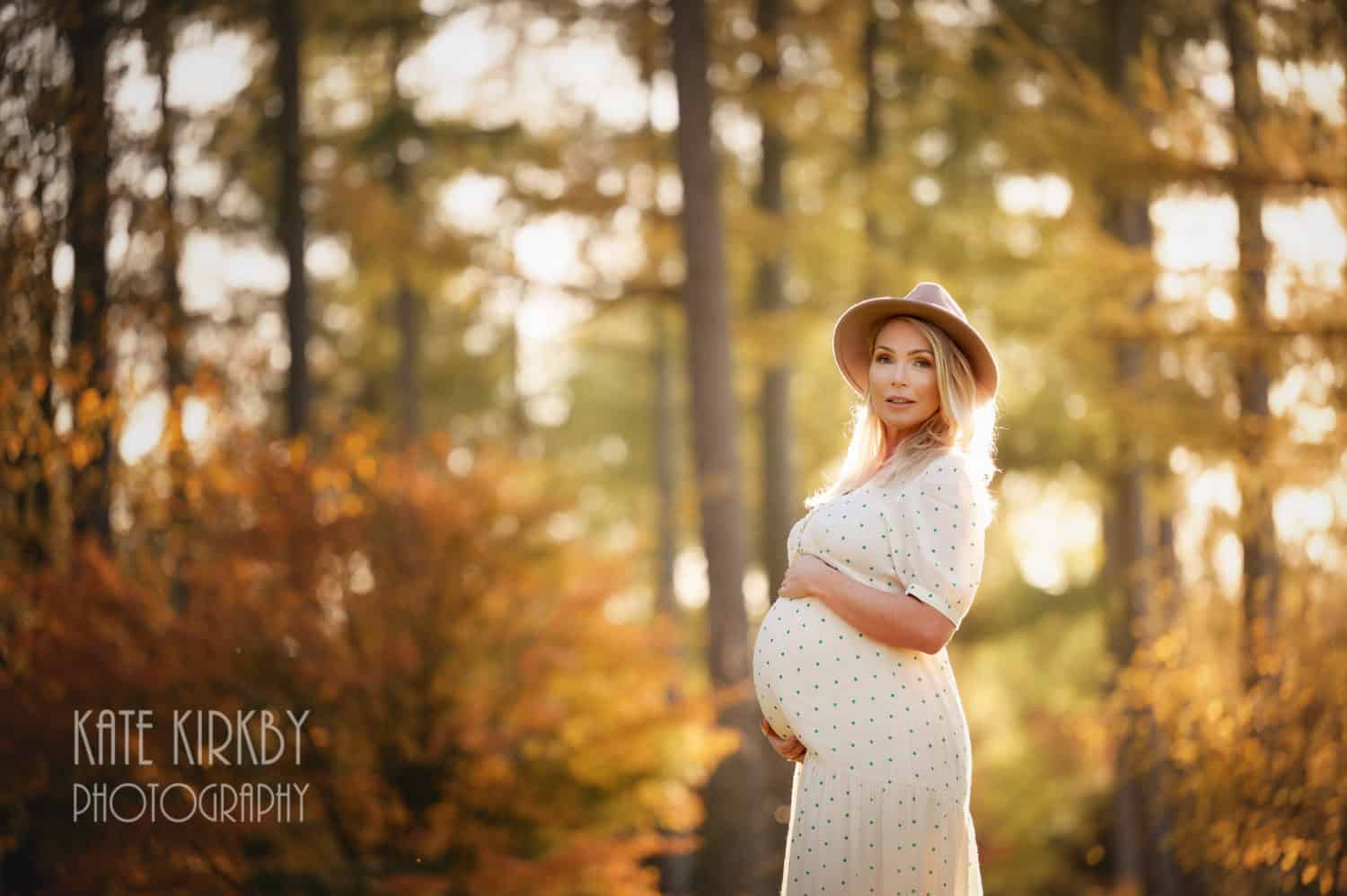 pregnant lady wearing summer dress and hat in woodland at golden hour