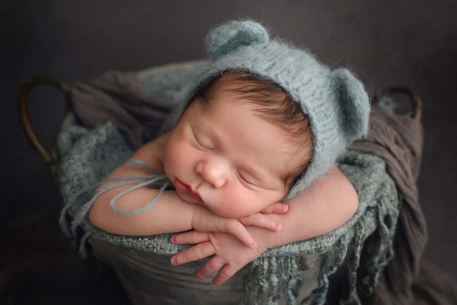 asleep newborn baby resting on his hands wearing an blue teddy ear hat