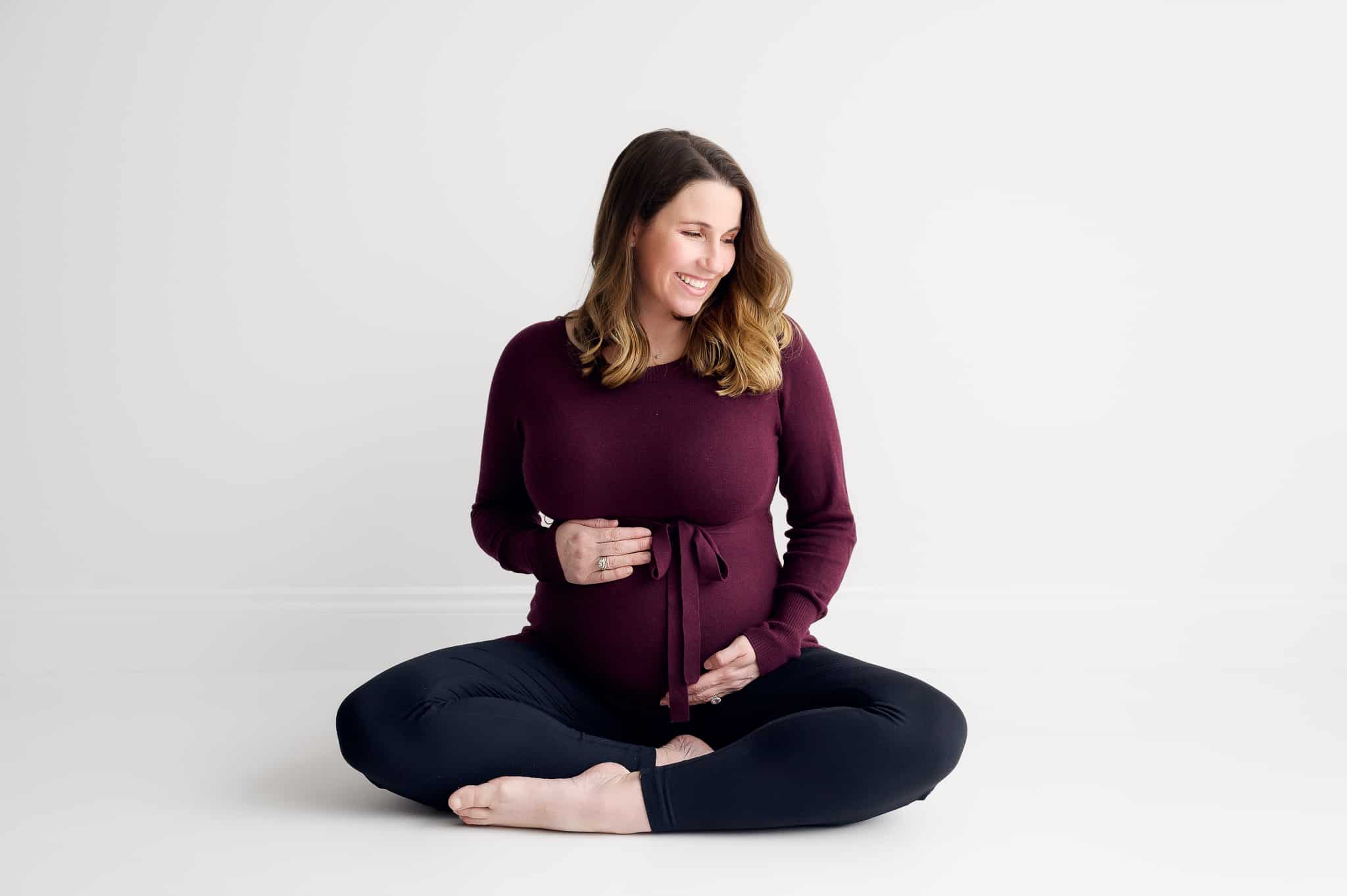 pregnant woman sitting cross legged touching her bump and smiling