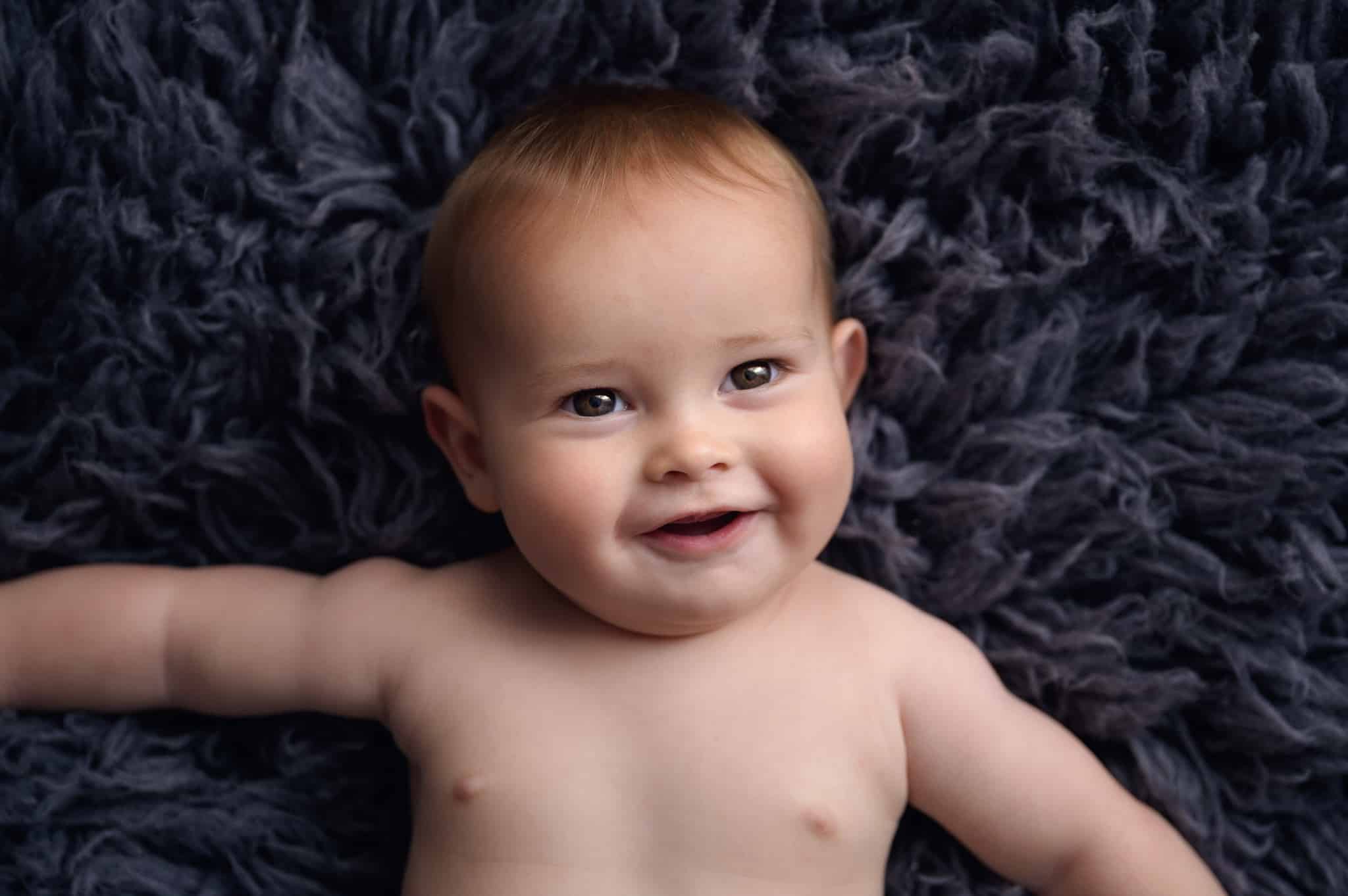 smiling baby lying on grey rug