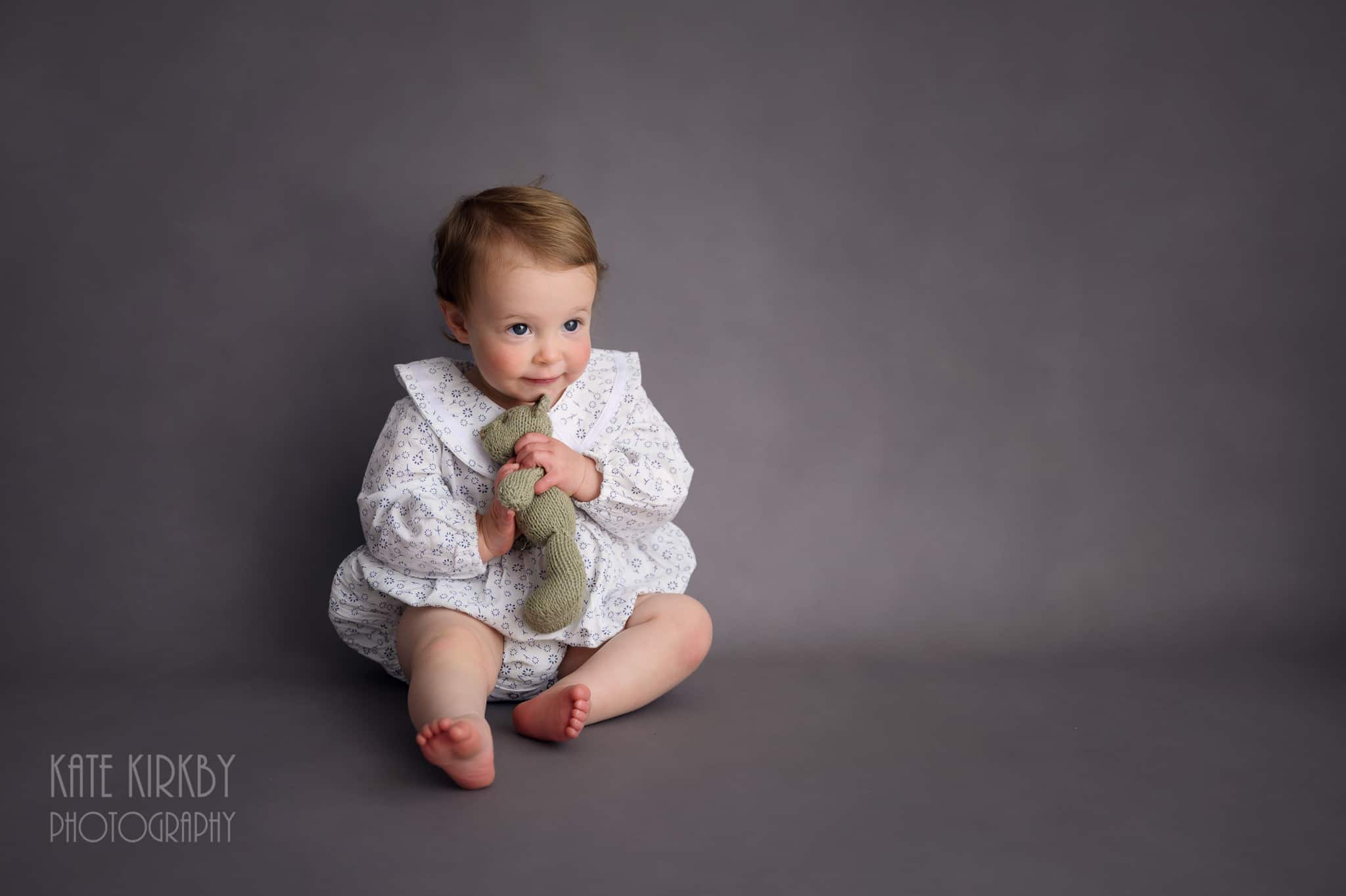 little girl smiling and sitting on grey back drop cuddling a little teddy