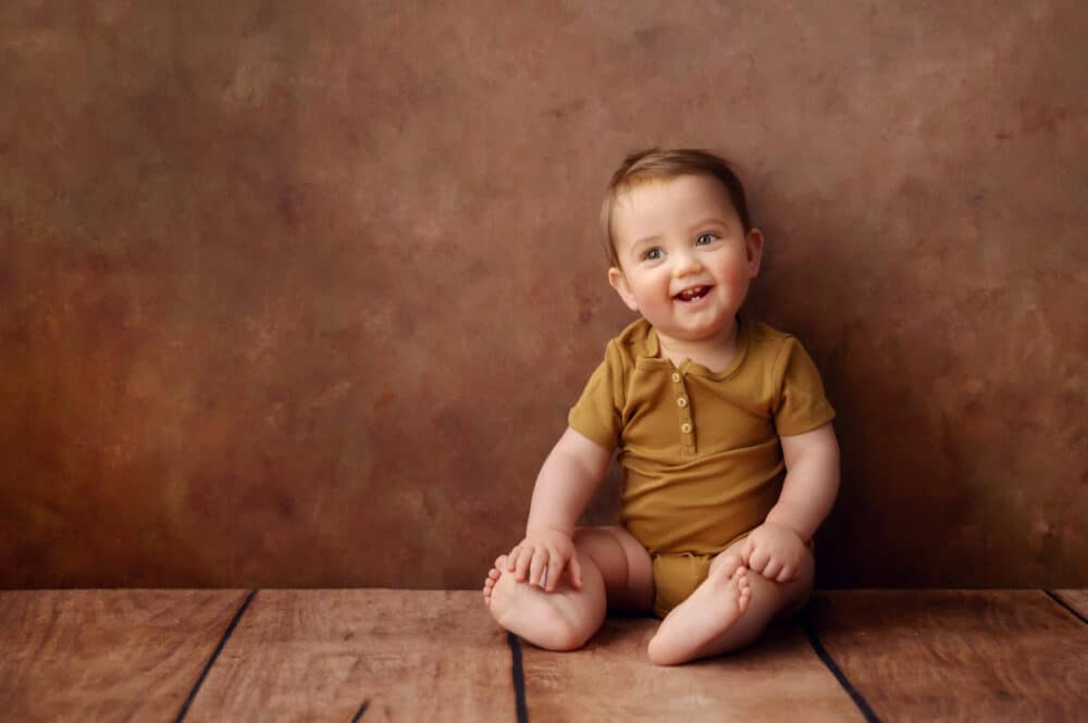 photograph of smiling baby sitting on wood floor in a studio in Bristol