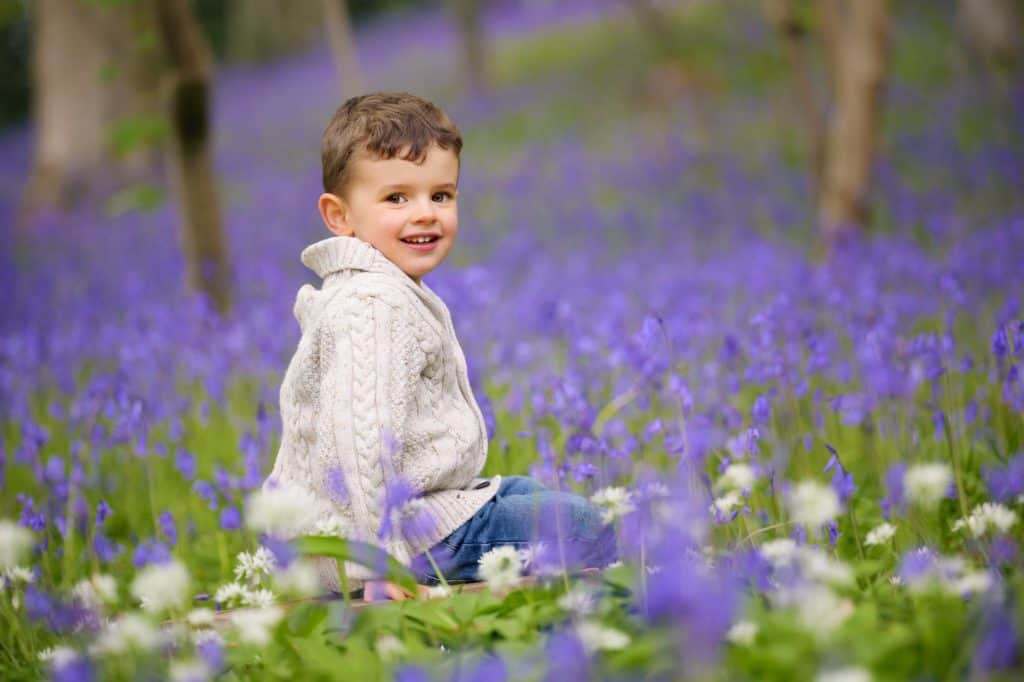 boy in cream cardigan sitting in bluebell woods in Bristol