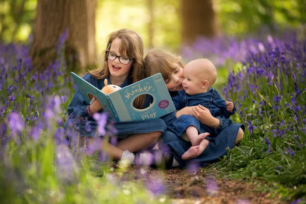 three sisters sitting in bluebell woods in Bristol reading a book