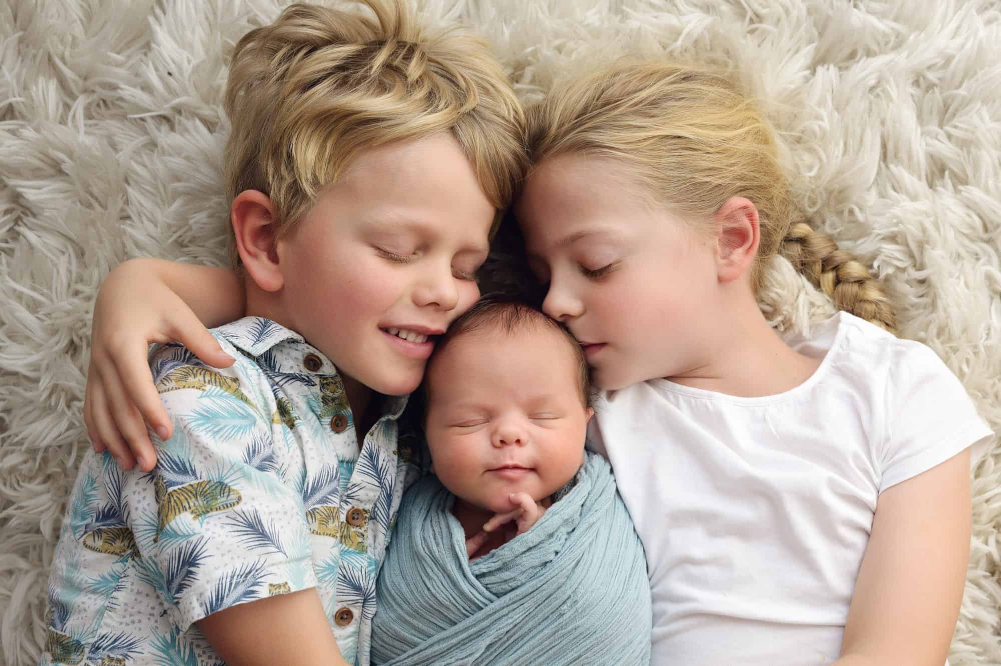siblings cuddling baby