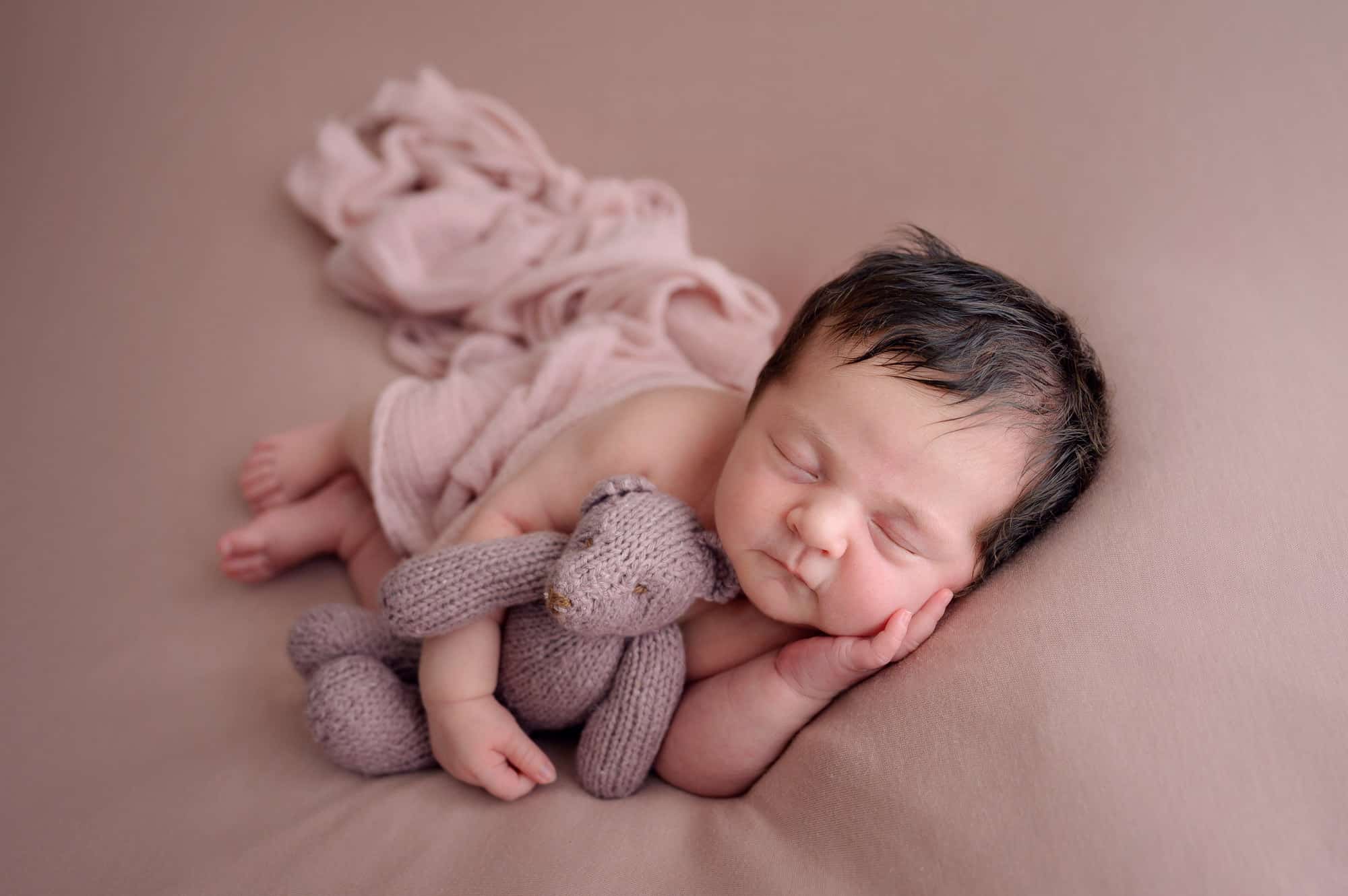 newborn baby cuddling pink teddy