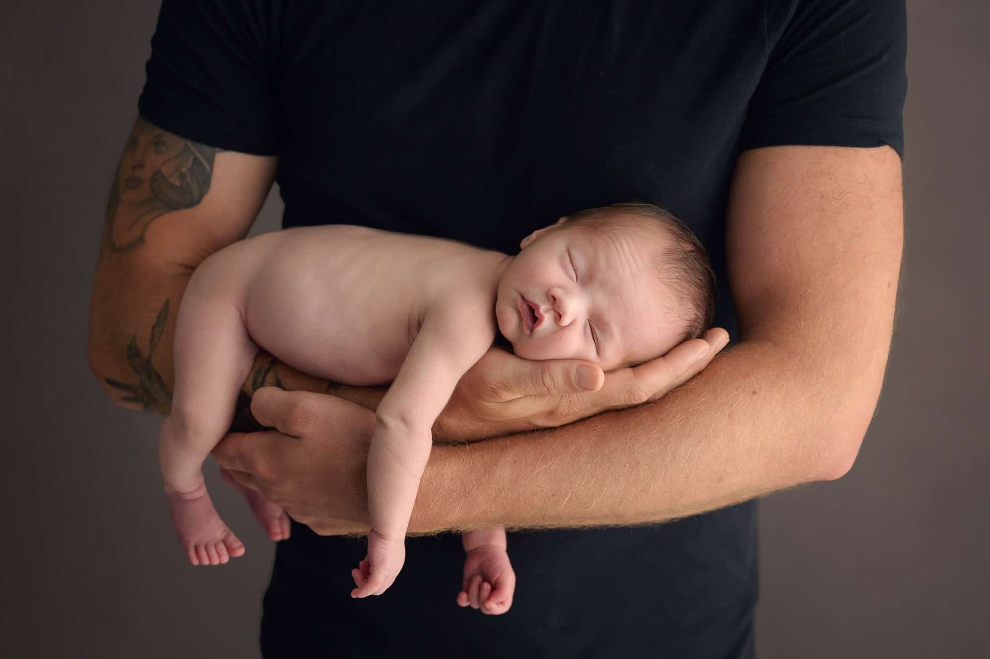 Newborn photograph of baby sleeping in dad's arms