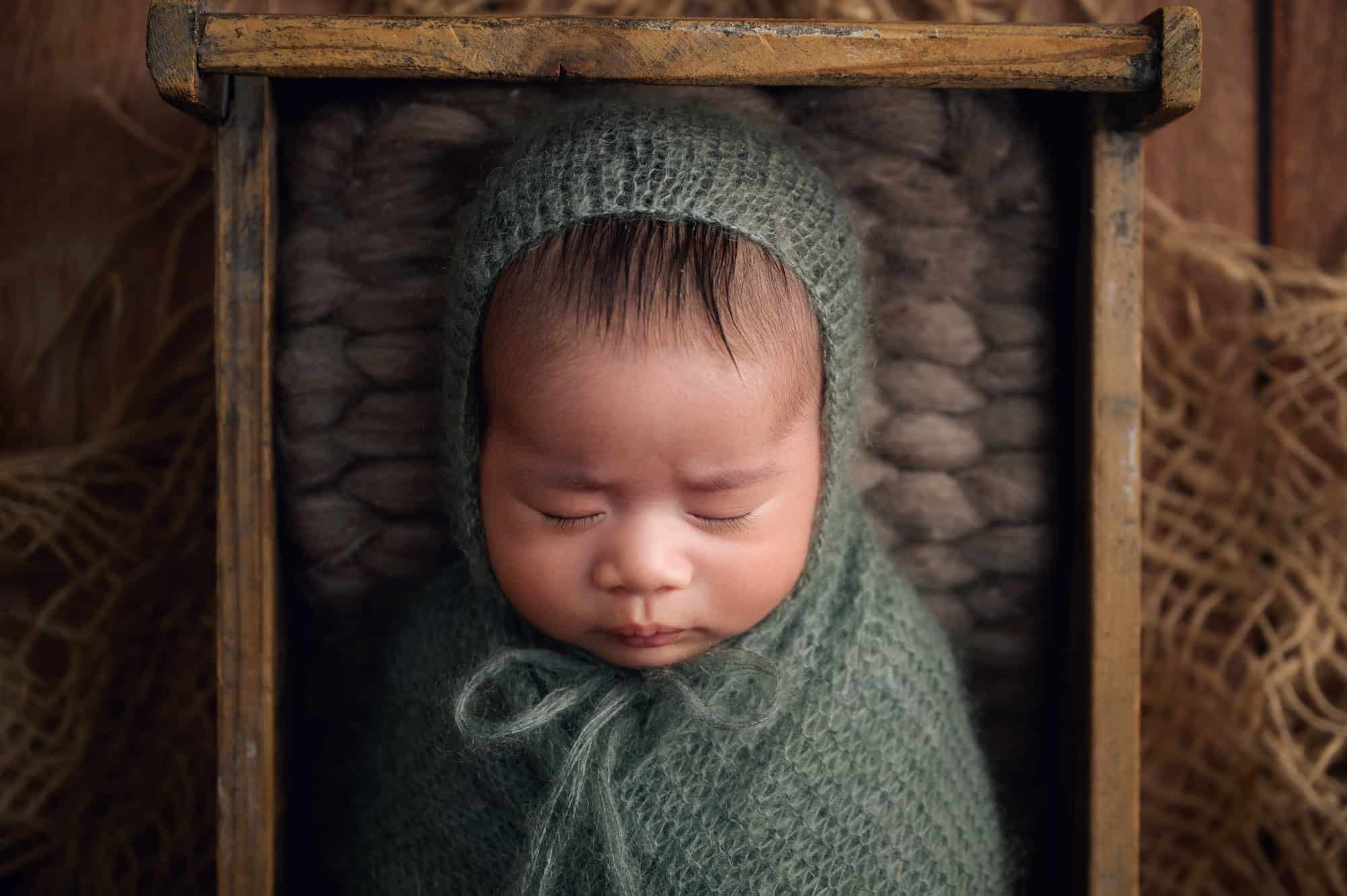 Newborn baby photograph in knitted green wrap and bonnet