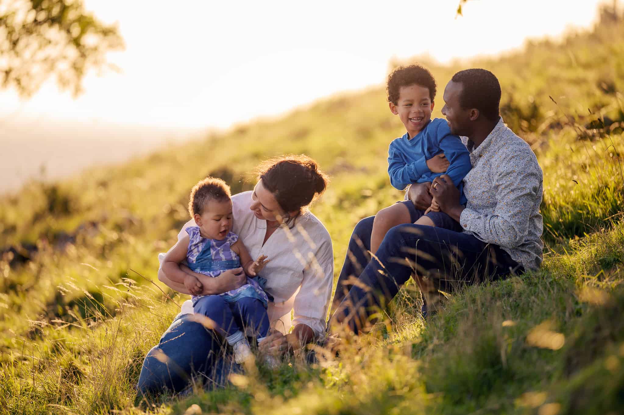 photograph of smiling family sitting in a field at sunset