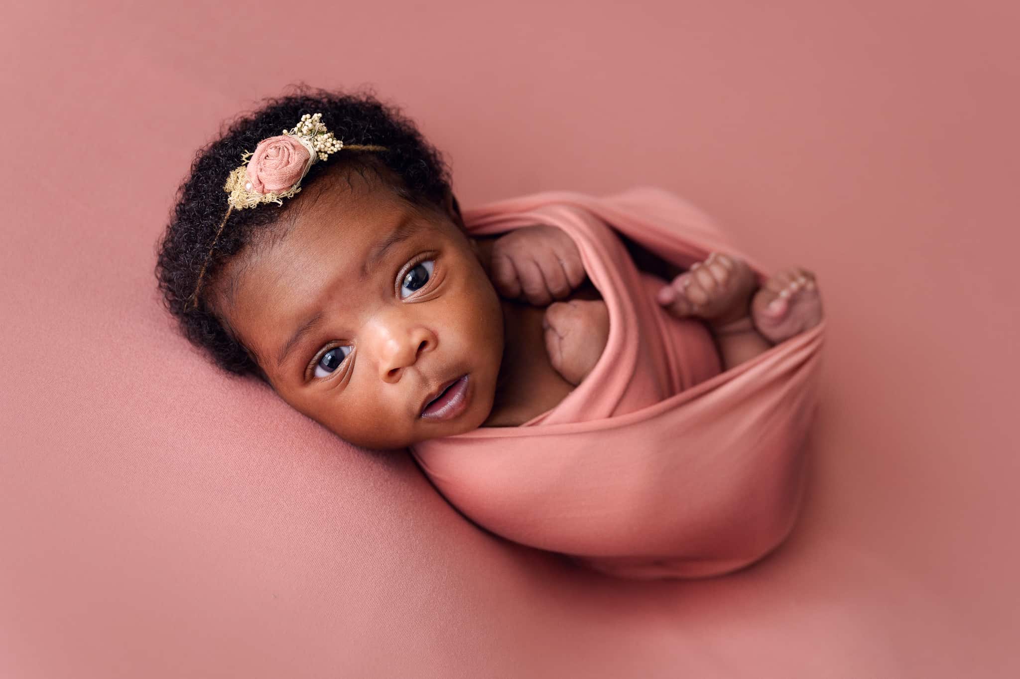 awake newborn baby in pink wrap