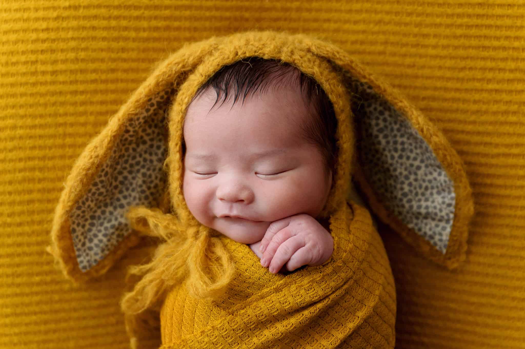 photo of newborn on mustard yellow with knitted bunny ear hat