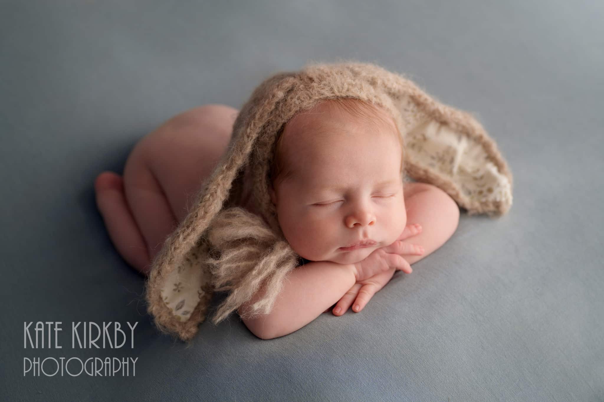 photo of newborn baby wearing an bunny hat with his head resting on his hands