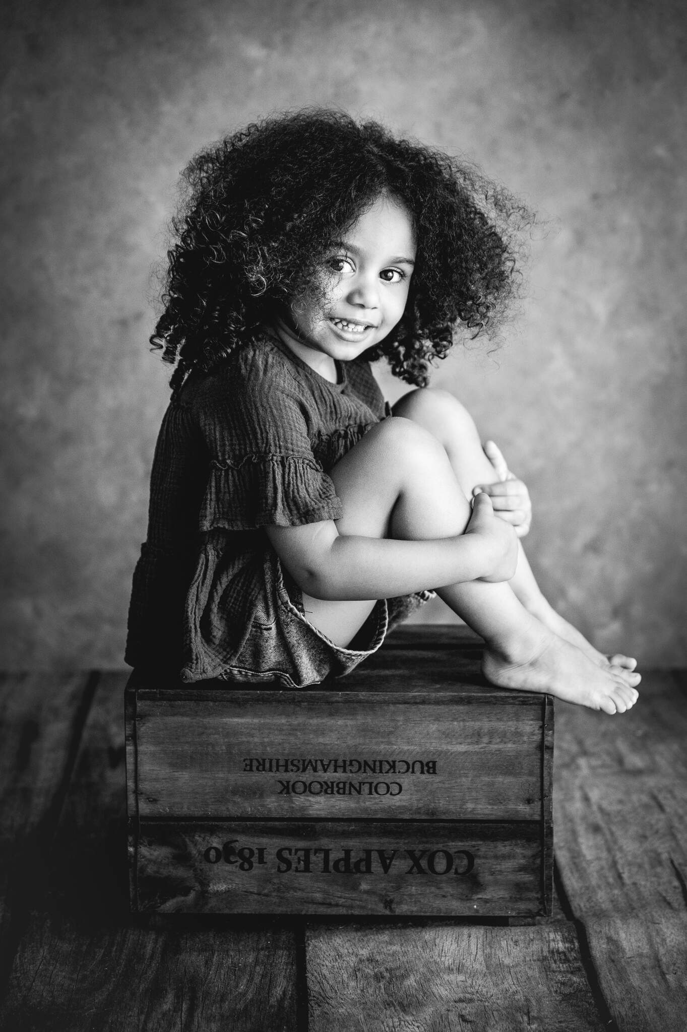 black & white studio photograph of girl sitting on a crate and smiling