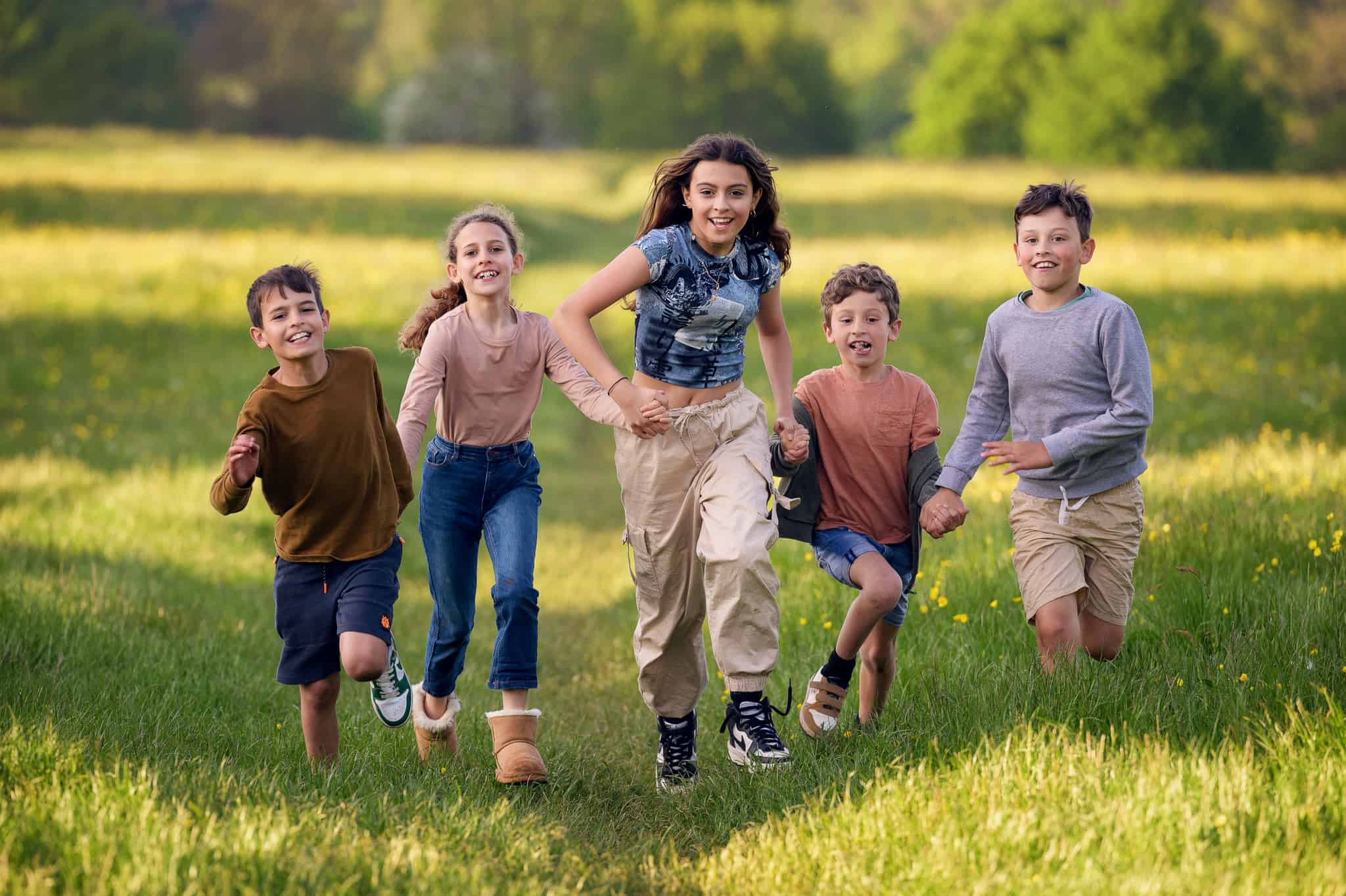 photograph of 5 smiling children holding hands running through a field