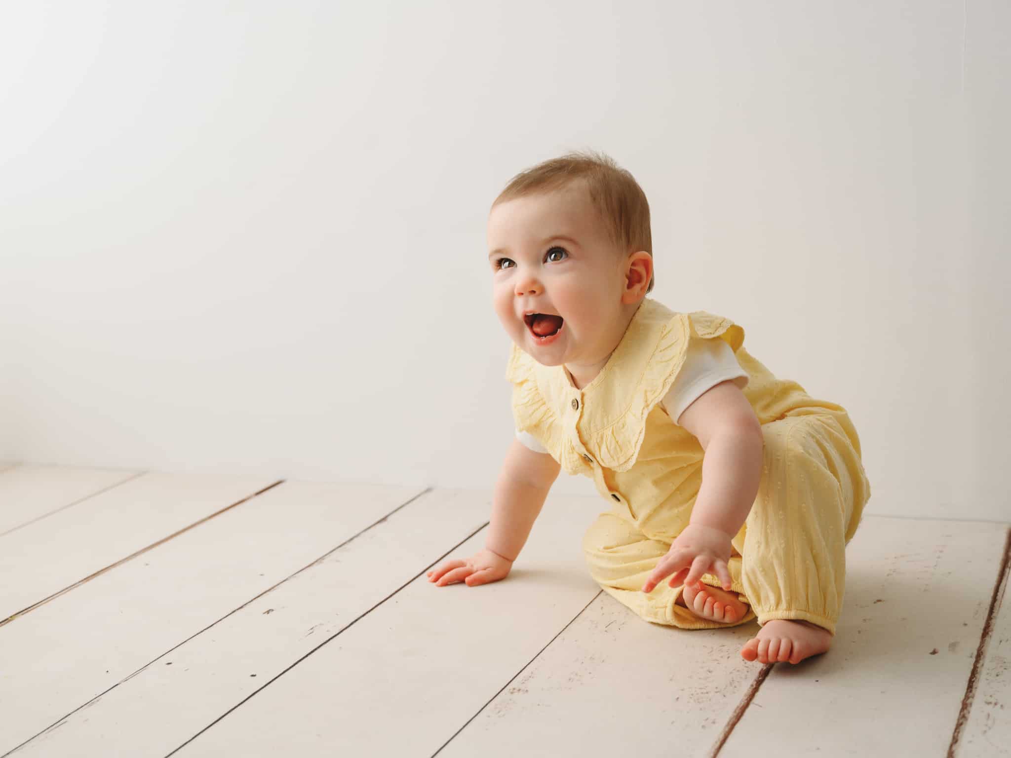 studio photograph of little girl wearing a yellow rompa in a white room