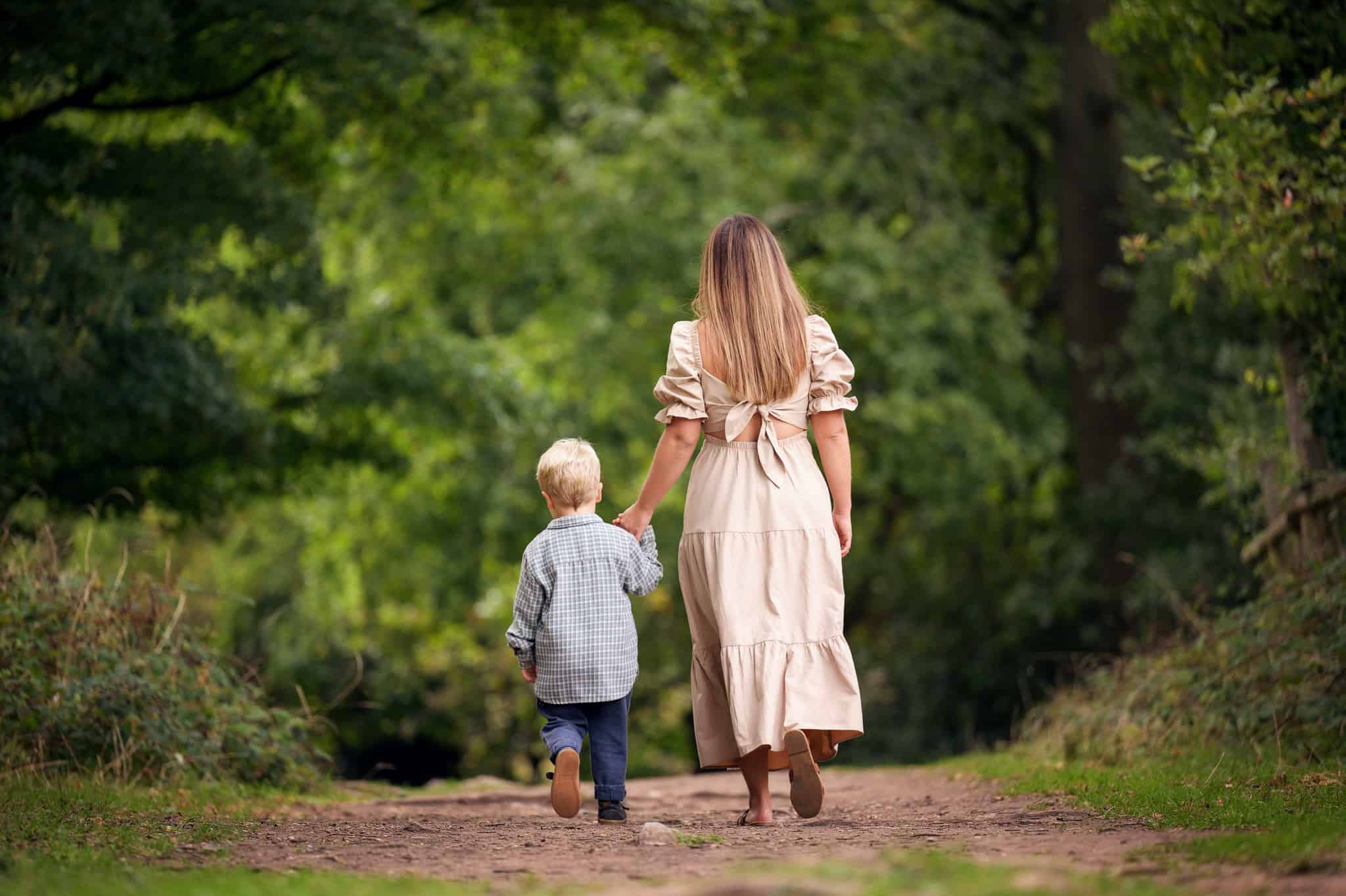 photograph of mother and son holding hands and walking away from the camera into the woods