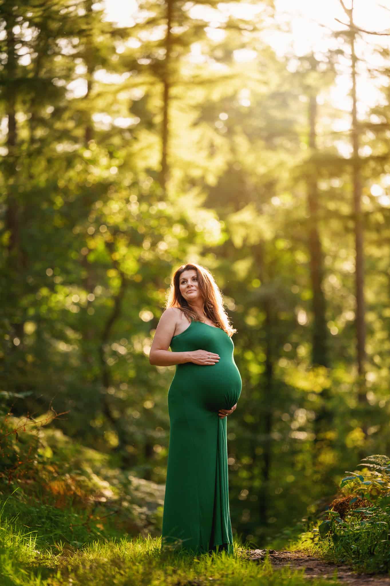 Maternity photo of lady wearing a green dress in a pine forest