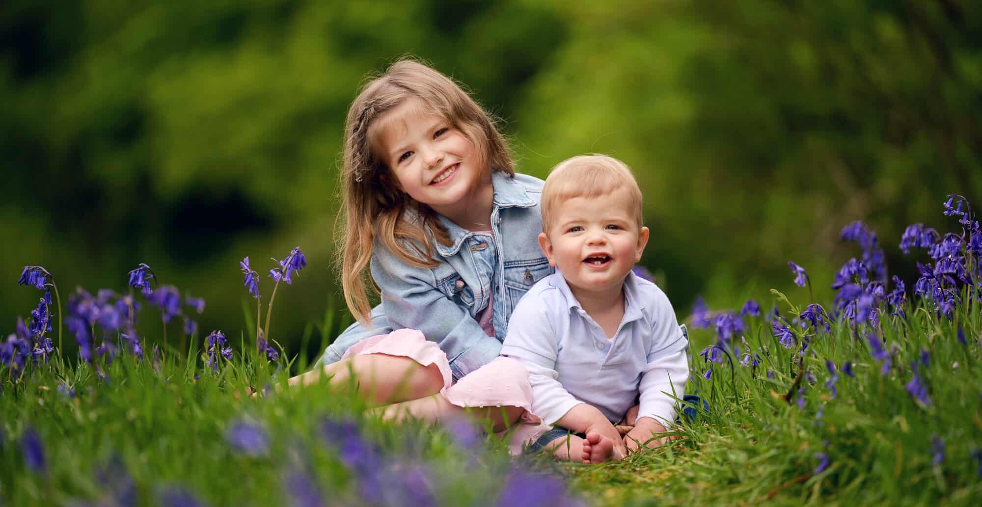 Beautiful family photograph of sister and baby brother sitting in a patch of bluebells.