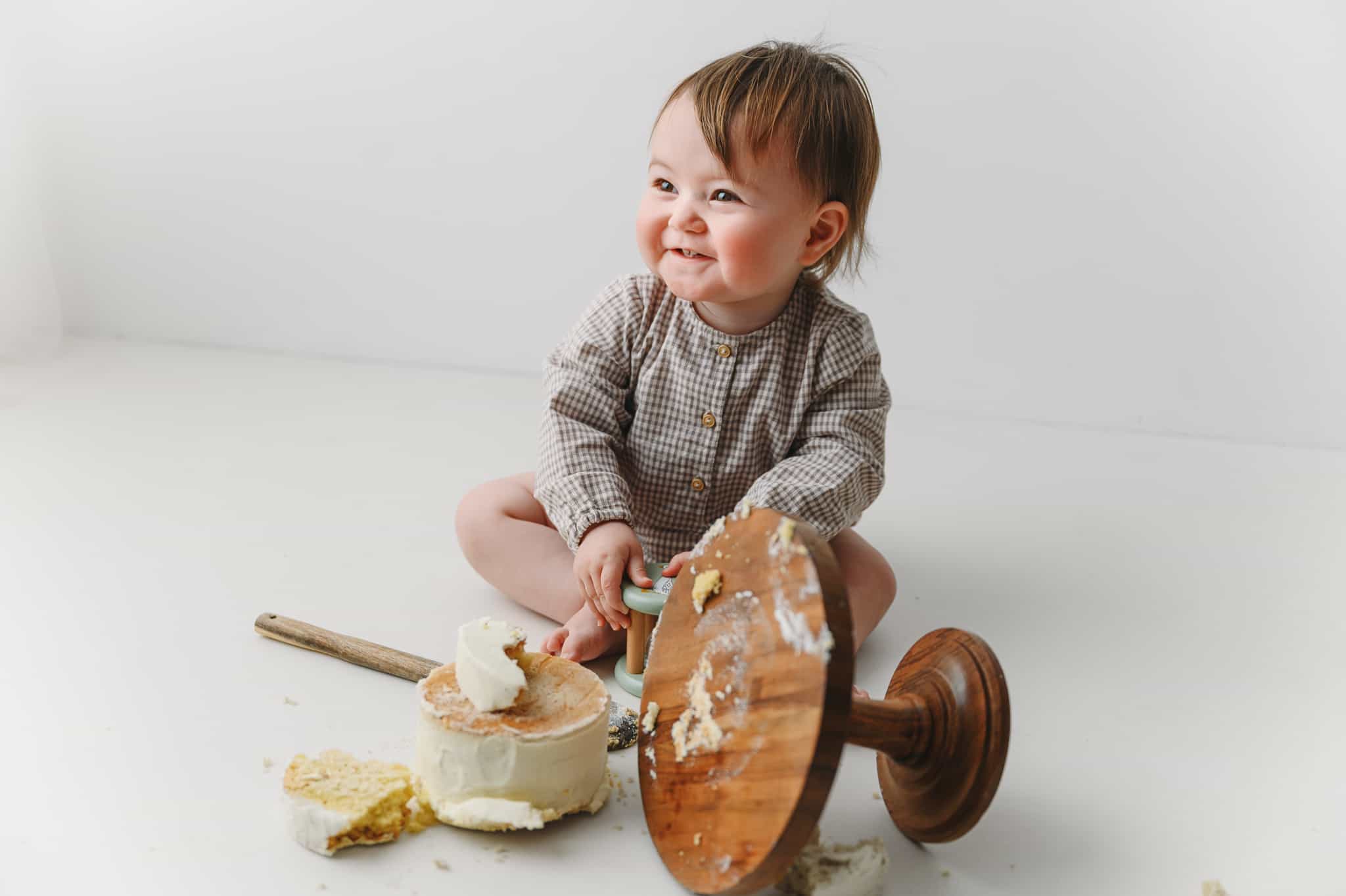 photo of a 1 year old girl smiling with smashed cake all over the floor